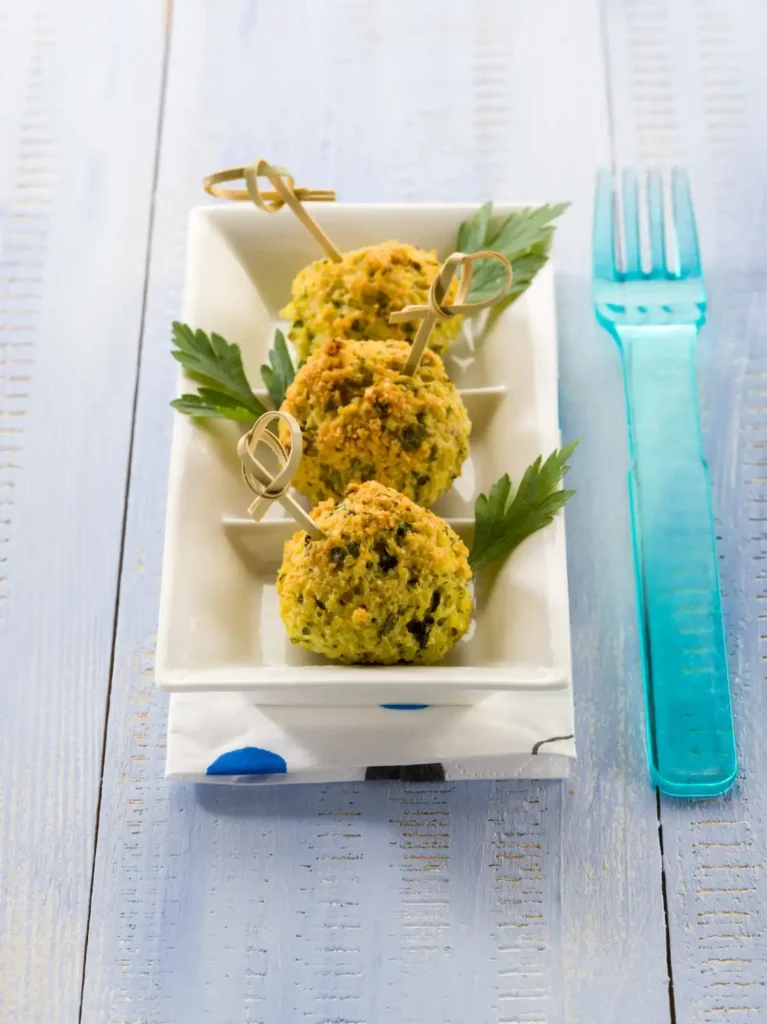 Golden baked vegetable balls served on skewers with parsley garnish on a rectangular white plate.