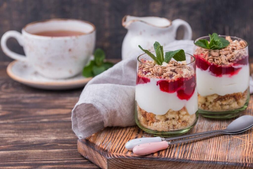 A layered apple parfait with yogurt, granola, and a hint of berry topping on a rustic wooden surface.